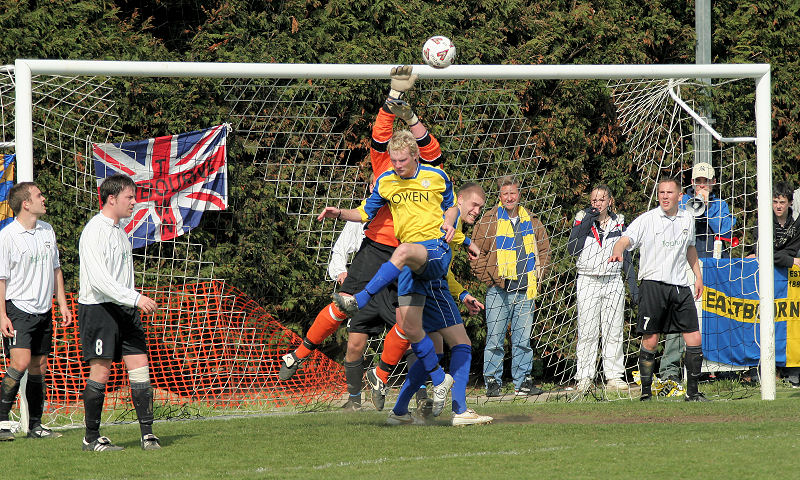 Steve Colbourne beats the ball away from two Eastbourne Town players in front of their fans
